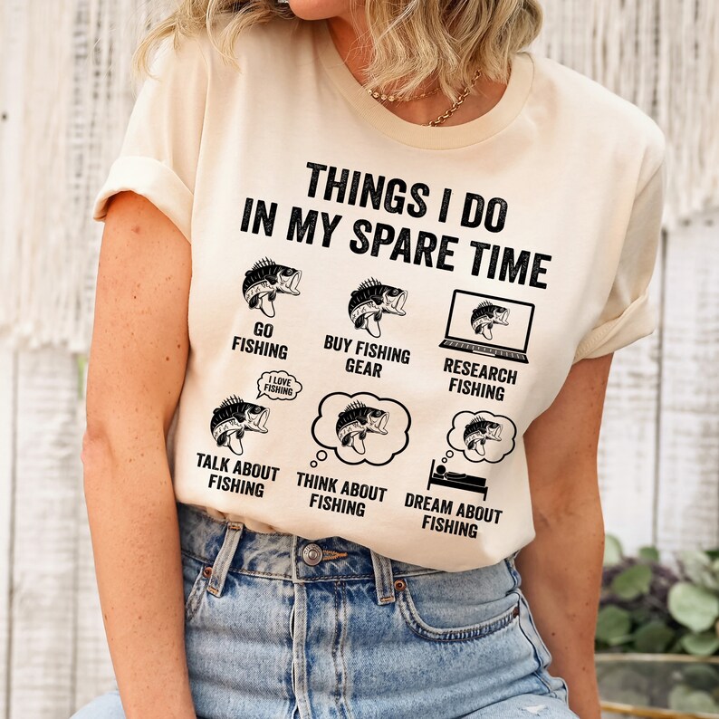 May include: A beige t-shirt with a black graphic that says "Things I do in my spare time" and lists activities related to fishing. The graphic includes illustrations of fish and fishing gear.