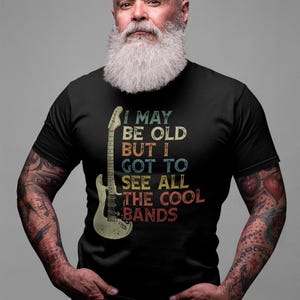 May include: A black t-shirt with a vintage-style graphic of a guitar and the text "I may be old but I got to see all the cool bands".