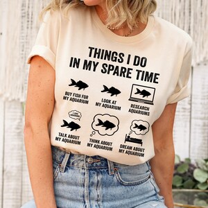 May include: A beige t-shirt with the text "Things I do in my spare time" and a list of activities related to aquariums, including "Buy fish for my aquarium", "Look at my aquarium", "Research aquariums", "Talk about my aquarium", "Think about my aquarium", and "Dream about my aquarium".