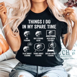 May include: Black t-shirt with white text that reads "Things I do in my spare time". The text is surrounded by illustrations of fish and fishing-related activities, including "Go Fishing", "Buy Fishing Gear", "Research Fishing", "Talk About Fishing", "Think About Fishing", and "Dream About Fishing".