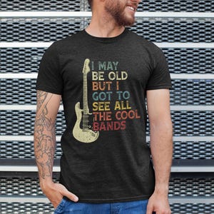 May include: A dark heather grey t-shirt with a vintage-style graphic of an electric guitar and the text "I may be old but I got to see all the cool bands".
