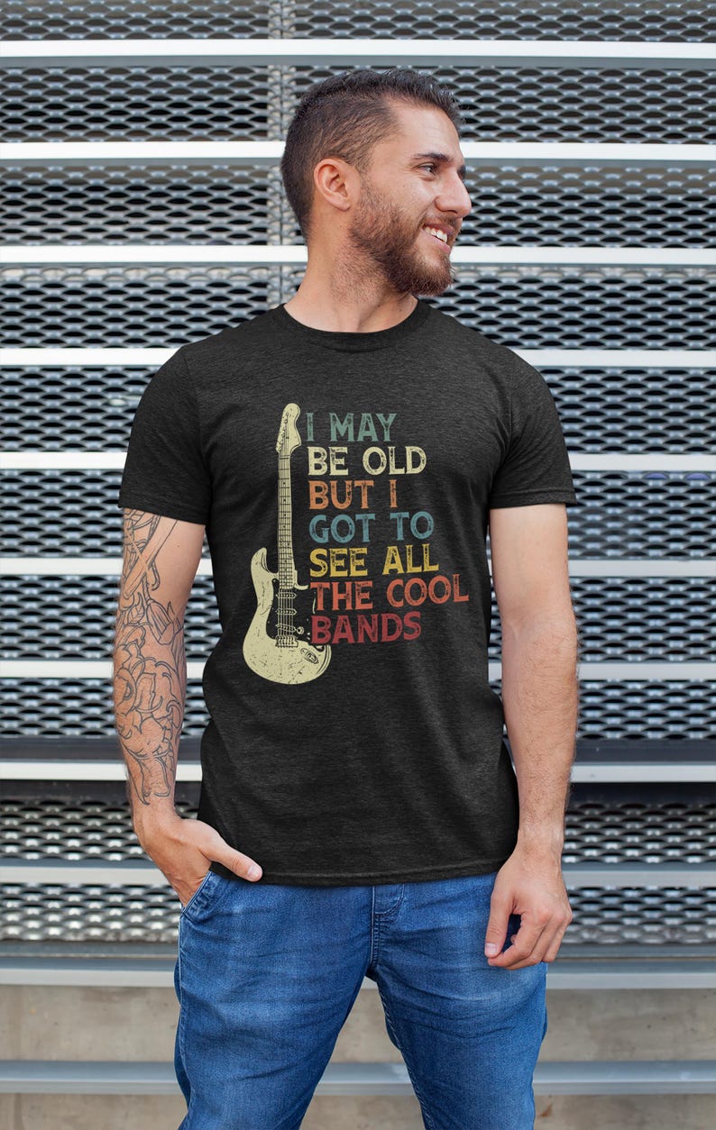 May include: A dark heather grey t-shirt with a vintage-style graphic of an electric guitar and the text "I may be old but I got to see all the cool bands".