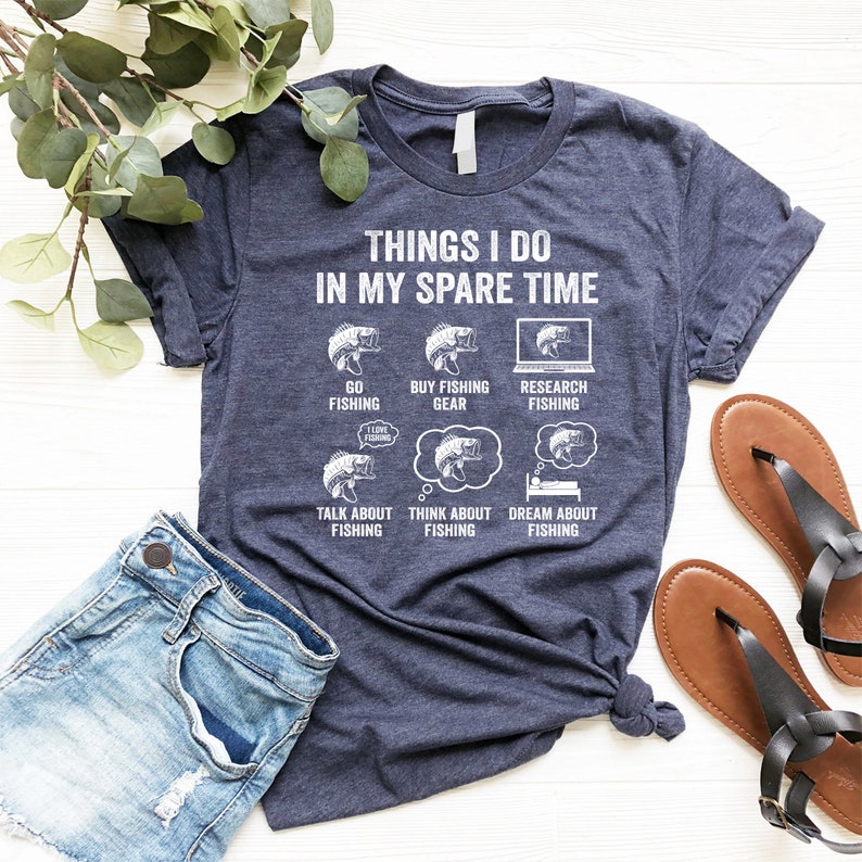 May include: A navy blue t-shirt with a white graphic that says "Things I do in my spare time" and shows a series of illustrations of fish and fishing related activities. The illustrations include: "Go Fishing", "Buy Fishing Gear", "Research Fishing", "Talk About Fishing", "Think About Fishing", and "Dream About Fishing".