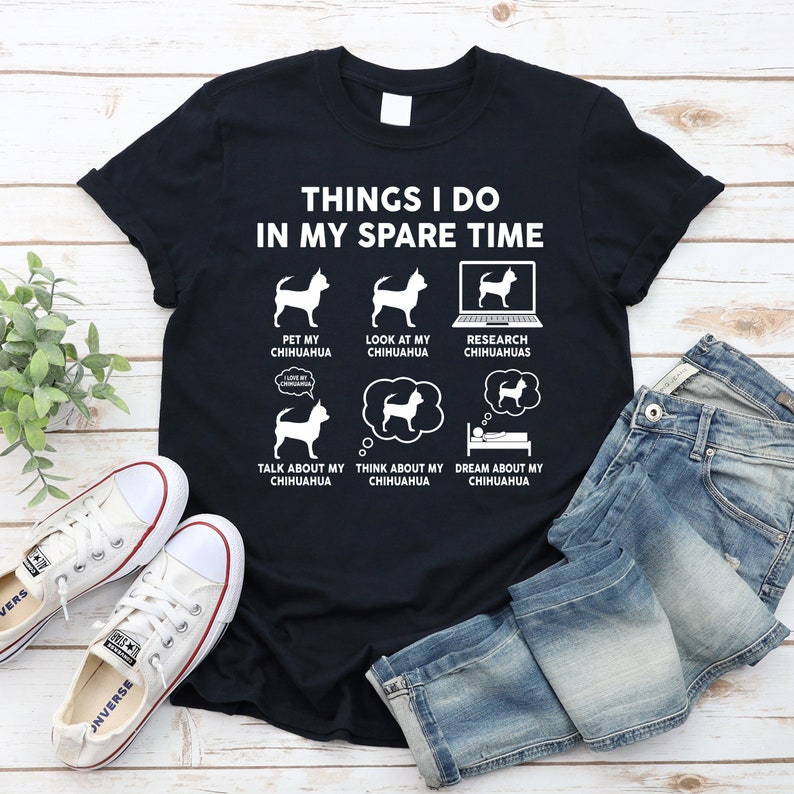 May include: A black t-shirt with white text that reads "Things I do in my spare time". The shirt features six illustrations of a chihuahua doing various activities, including petting, looking at a computer, thinking, and sleeping.