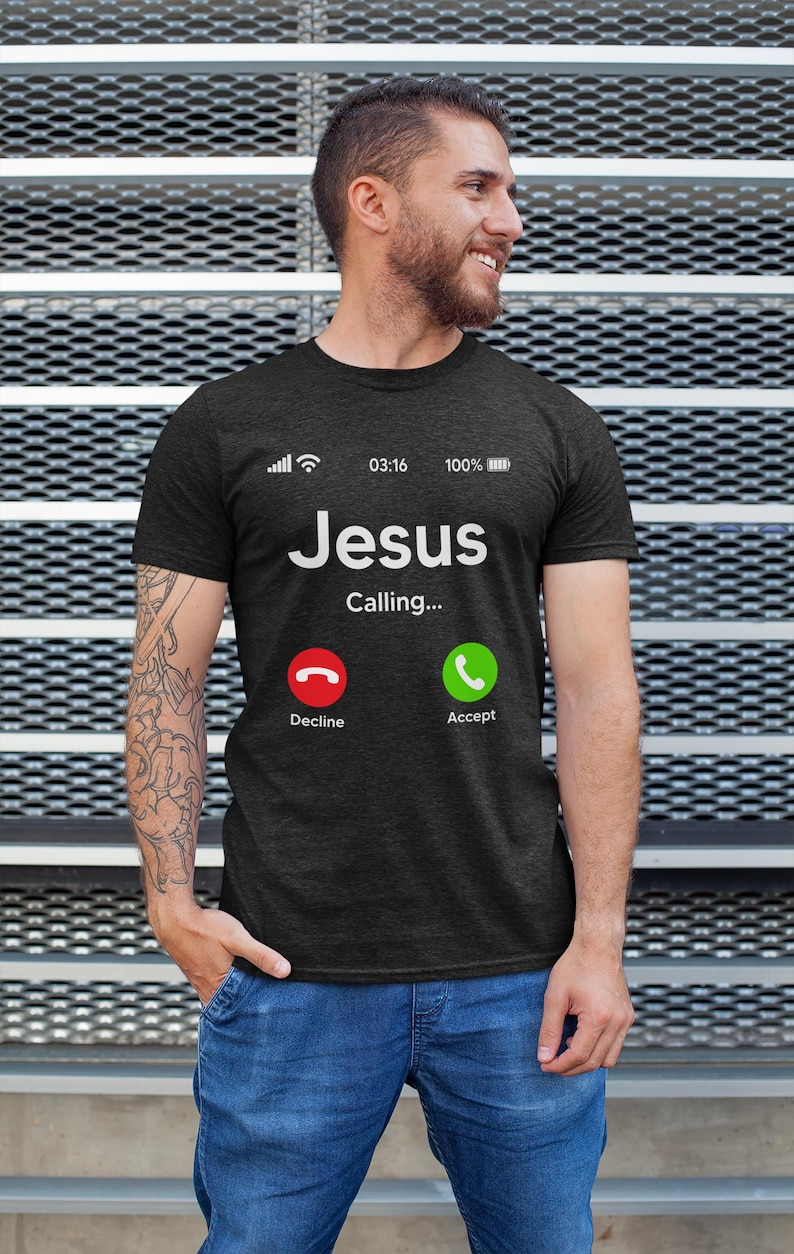 May include: A dark grey t-shirt with a white graphic of a phone screen. The screen displays "Jesus Calling..." with a red decline button and a green accept button.