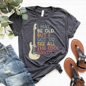 May include: A dark grey t-shirt with a vintage-style graphic of an electric guitar and the text "I may be old but I got to see all the cool bands".