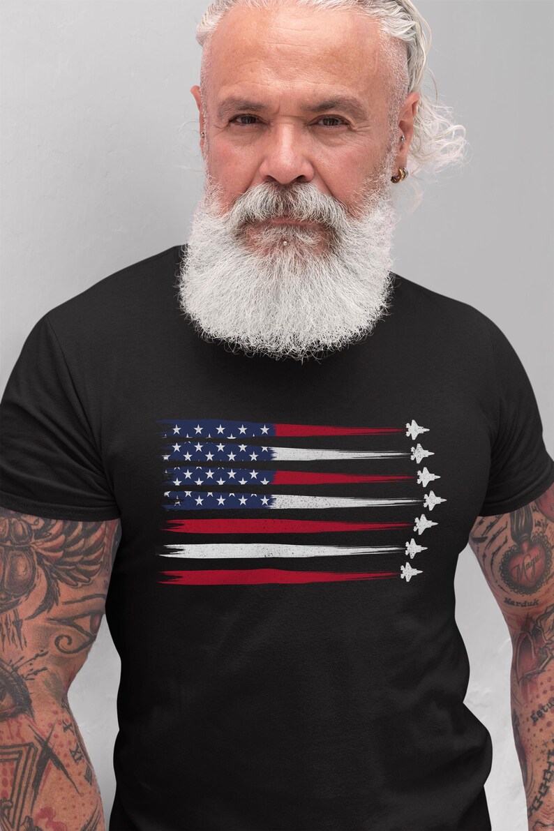 Puede incluir: Una camiseta negra con un dise&ntilde;o de bandera estadounidense desgastado que presenta una fila de aviones de combate volando en formaci&oacute;n.