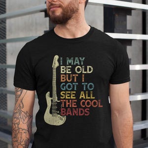 May include: A black t-shirt with a vintage-style graphic of an electric guitar and the text "I may be old but I got to see all the cool bands".