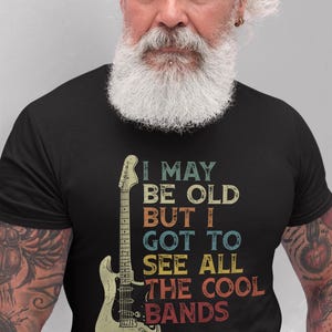 May include: A black t-shirt with a vintage-style graphic of a guitar and the text "I may be old but I got to see all the cool bands".