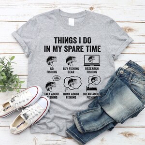 May include: A gray t-shirt with the text "Things I do in my spare time" and illustrations of fish. The illustrations depict activities like going fishing, buying fishing gear, researching fishing, talking about fishing, thinking about fishing, and dreaming about fishing.