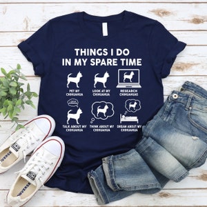 May include: A navy blue t-shirt with a white graphic that says "Things I do in my spare time" and features a series of illustrations of a chihuahua dog. The illustrations show the dog being petted, looked at, researched, talked about, thought about, and dreamed about.