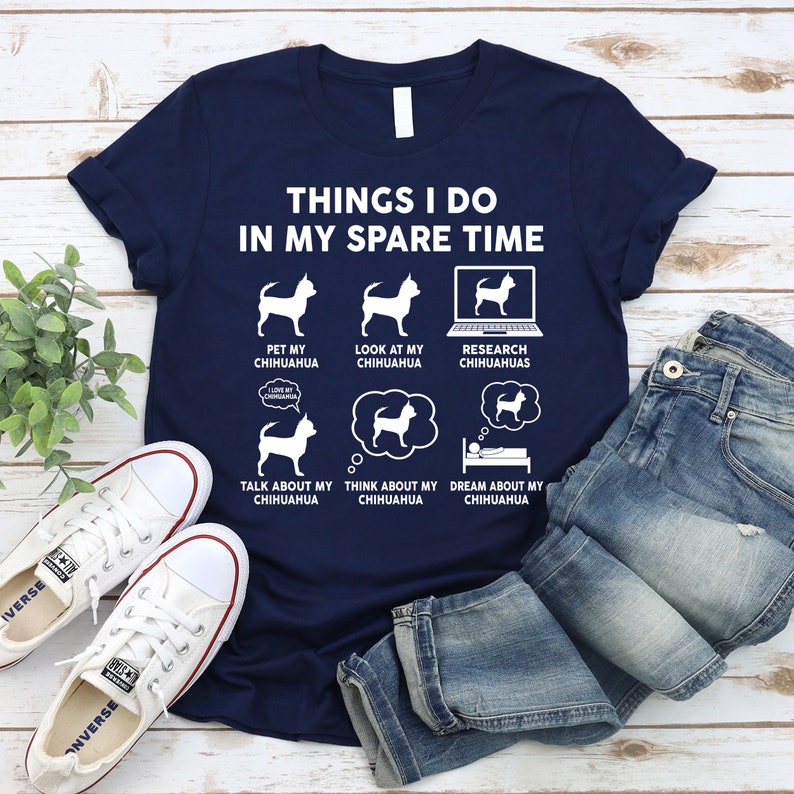 May include: A navy blue t-shirt with a white graphic that says "Things I do in my spare time" and features a series of illustrations of a chihuahua dog. The illustrations show the dog being petted, looked at, researched, talked about, thought about, and dreamed about.