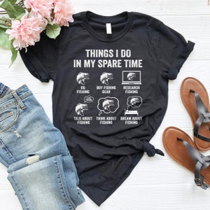 May include: A black t-shirt with a white graphic that says "Things I do in my spare time" and lists activities related to fishing. The graphic includes illustrations of fish, fishing gear, and a laptop.