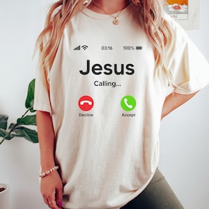 May include: A white t-shirt with a graphic of a phone screen that says "Jesus Calling..." with a red decline button and a green accept button.