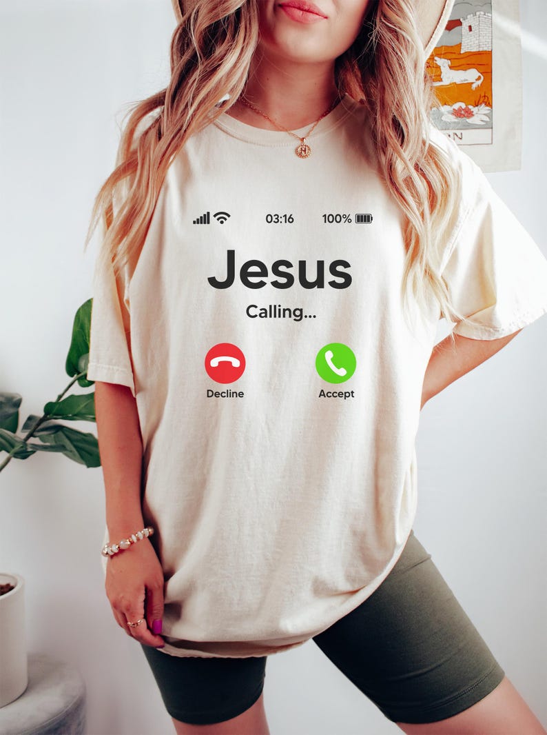 May include: A white t-shirt with a graphic of a phone screen that says "Jesus Calling..." with a red decline button and a green accept button.