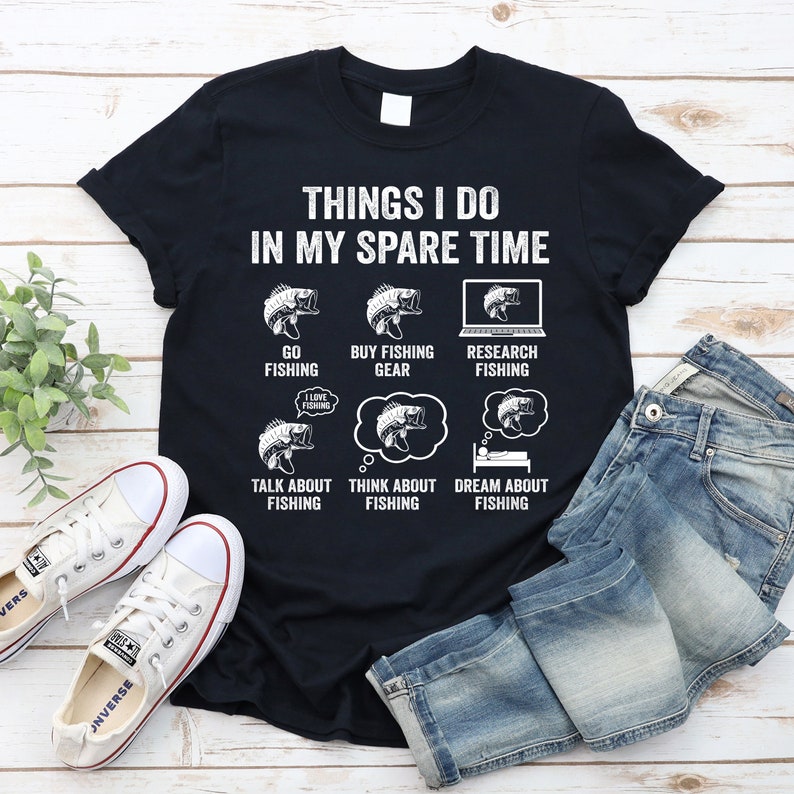 May include: A black t-shirt with white text that reads "Things I do in my spare time". The text is arranged in a list with illustrations of fish and fishing gear. The list includes "Go Fishing", "Buy Fishing Gear", "Research Fishing", "Talk About Fishing", "Think About Fishing", and "Dream About Fishing".