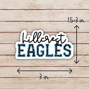 May include: Black and blue vinyl sticker with the text "Hillcrest Eagles" in a sparkly font. The sticker is 3 inches wide and 1.5 inches tall.