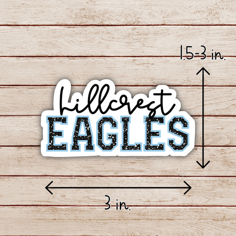 May include: Black and blue vinyl sticker with the text "Hillcrest Eagles" in a sparkly font. The sticker is 3 inches wide and 1.5 inches tall.