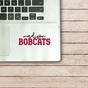 May include: A red and white sticker with the text "madison BOBCATS" on a silver laptop.