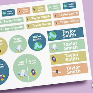 Puede incluir: Una hoja de etiquetas adhesivas con el nombre Taylor Smith en texto blanco. Las pegatinas vienen en varias formas, incluyendo rectángulos y círculos, decoradas con gráficos de temática espacial como cohetes, planetas y satélites en tonos suaves.