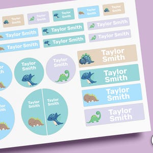Puede incluir: Una hoja de etiquetas adhesivas con varias ilustraciones de dinosaurios y el nombre Taylor Smith impreso en blanco. Las pegatinas tienen formas rectangulares y circulares en tonos azul, verde y beige, con el texto STICK-ON visible.