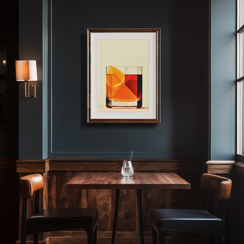 May include: A framed art print depicting a cocktail with an orange slice. The artwork is displayed on a dark teal wall above a wooden table with two chairs. A wall sconce and a window are also visible.