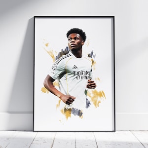 Può includere: Stampa artistica incorniciata raffigurante un calciatore con una maglia bianca con la scritta "Emirates Fly Better". L'opera d'arte ha un effetto acquerello con accenti oro e grigio. La stampa è incorniciata in una cornice nera.