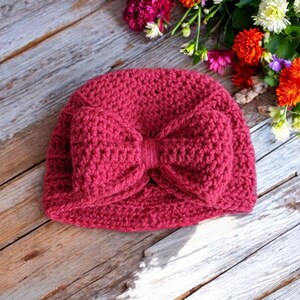 May include: A crocheted beanie with a large, pink bow. The beanie is made of a soft, textured yarn and is perfect for keeping warm in the winter.