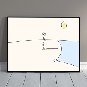 Puede incluir: Lámina artística minimalista enmarcada con un dibujo lineal negro de una persona en la playa, con un sol amarillo. La obra de arte está sobre un fondo crema con un océano azul y un marco negro.