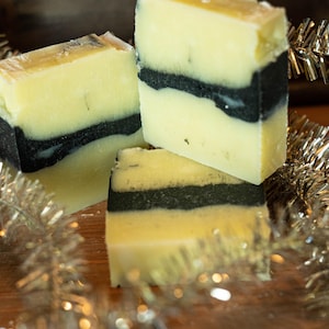 May include: Three bars of handmade soap with a black and white swirl design. The soap is sitting on a wooden surface with silver tinsel.