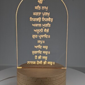 Puede incluir: Luz de noche acr&iacute;lica iluminada con texto grabado. La luz est&aacute; montada sobre una base de madera redonda. El texto es de color dorado y est&aacute; iluminado por la luz.