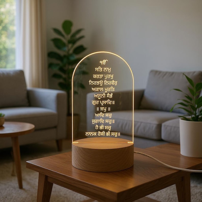 Puede incluir: L&aacute;mpara LED con base de madera y panel de acr&iacute;lico transparente arqueado. El panel muestra texto dorado e iluminado con un brillo c&aacute;lido. La l&aacute;mpara est&aacute; sobre una mesa de madera.