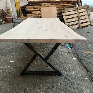 May include: A whitewashed wood table top with a live edge and a black metal X-shaped base.
