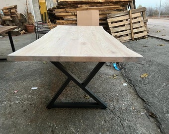 May include: A whitewashed wood table top with a live edge and a black metal X-shaped base.