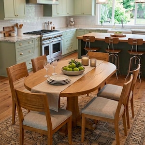 May include: An oval wooden dining table with four chairs featuring light gray upholstered seats. The table is set with a beige runner, a bowl of green apples, two wine glasses, and two plates. The setting is placed on a patterned area rug.