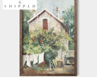 May include: A vintage painting of a stone house with a red door and a clothesline with white laundry hanging in the yard. The house is surrounded by green trees and bushes. The painting is framed in a brown wood frame.