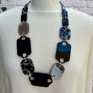 May include: A black and white statement necklace with large, rectangular, patterned beads. The necklace is made of plastic and has a shiny finish.