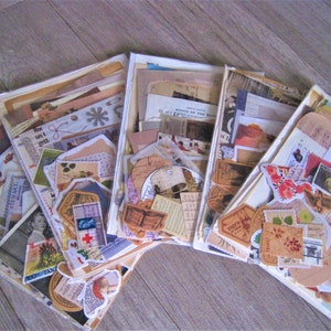 Puede incluir: Cinco bolsas de pl&aacute;stico transparentes llenas de ef&iacute;meras vintage, incluyendo recortes de papel, postales, sellos y papel decorativo. Las ef&iacute;meras son de varios tonos de marr&oacute;n, rojo y blanco.