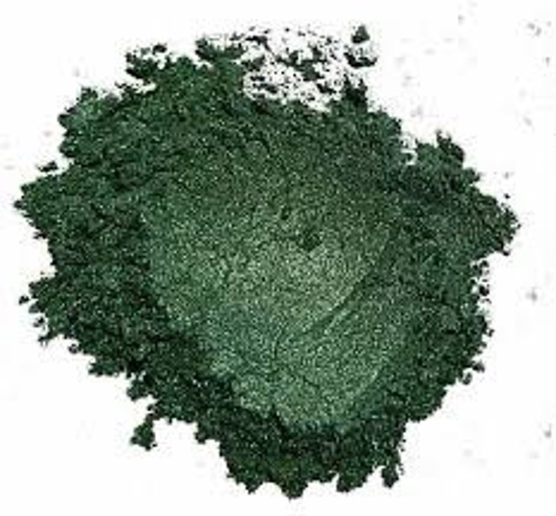 May include: A close-up of a pile of dark green mica powder. The powder has a shimmery, metallic finish.