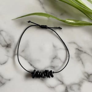 May include: A black bracelet with a black cord and black stone beads.