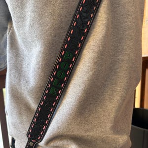 May include: Black leather bag strap with embossed floral design and pink stitching. The word "POOLE" is displayed in green lettering. The strap is attached to a bag with a silver clasp.