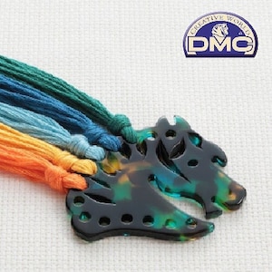 Puede incluir: Un conjunto de hilo de bordar multicolor enrollado alrededor de un organizador de hilo de plástico verde y negro con forma de dos cabezas de animales estilizadas.