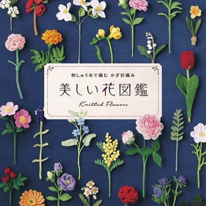 以下が含まれることがあります： 日本語と英語で「美しい花図鑑」というタイトルの書籍の表紙。表紙には、バラ、ユリ、デイジーなど、さまざまな色とスタイルの編み物でできた花が、青い背景に配置されています。