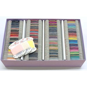 May include: A box filled with spools of colorful thread, neatly arranged in rows. The threads are in a variety of colors, including pink, yellow, blue, and green. A few spools are loose in the box. The box is a light purple color.