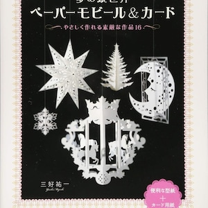 Puede incluir: Portada de libro con móviles y tarjetas de papel blanco. El título está en japonés, con las palabras "Paper Mobile & Card" en inglés. La portada muestra varios diseños recortados en papel, incluyendo una estrella, un árbol, una luna y un carrusel.