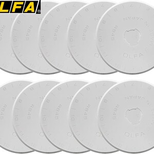 May include: A collection of white OLFA RB45 rotary cutter replacement blades. Each blade is round with a central hole and marked with numbers and the text "RB45" and "MADE IN JAPAN". The OLFA logo is in the top left corner.