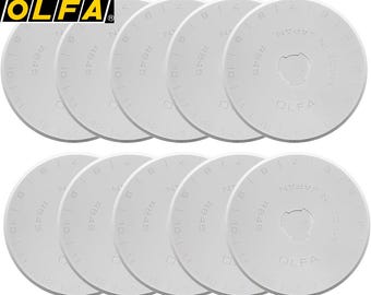 Puede incluir: Un conjunto de cuchillas de repuesto blancas OLFA RB45 para cortadores rotativos. Cada cuchilla circular tiene un orificio central y está marcada con números, el texto "RB45" y "MADE IN JAPAN". El logotipo de OLFA está en la esquina superior izquierda.