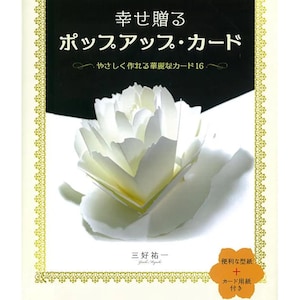 以下が含まれることがあります： 白いペーパーフラワーと日本語のテキストが特徴の書籍の表紙。タイトルは「幸せ贈るポップアップ・カード」です。表紙には金色の縁取りがあり、作りやすいカードとカードテンプレートに関するテキストが含まれています。