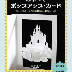 Puede incluir: Tarjeta desplegable blanca con diseño de castillo, sobre fondo negro. La tarjeta está abierta, revelando un castillo de papel detallado sobre formas de nubes. Texto japonés visible en la portada.