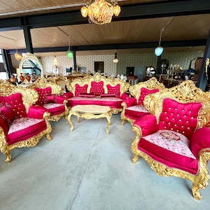 Op de afbeelding: Een luxe woonkamerset met sierlijke goudkleurige frames en levendige rode fluwelen bekleding. De set bevat een bank, fauteuils en een salontafel, allemaal met gedetailleerde gravures en gecapitonneerde kussens. De meubels zijn opgesteld in een ruime kamer.